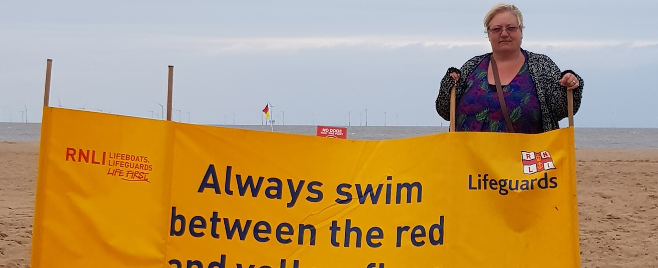 A woman on a beach with an RNLI banner